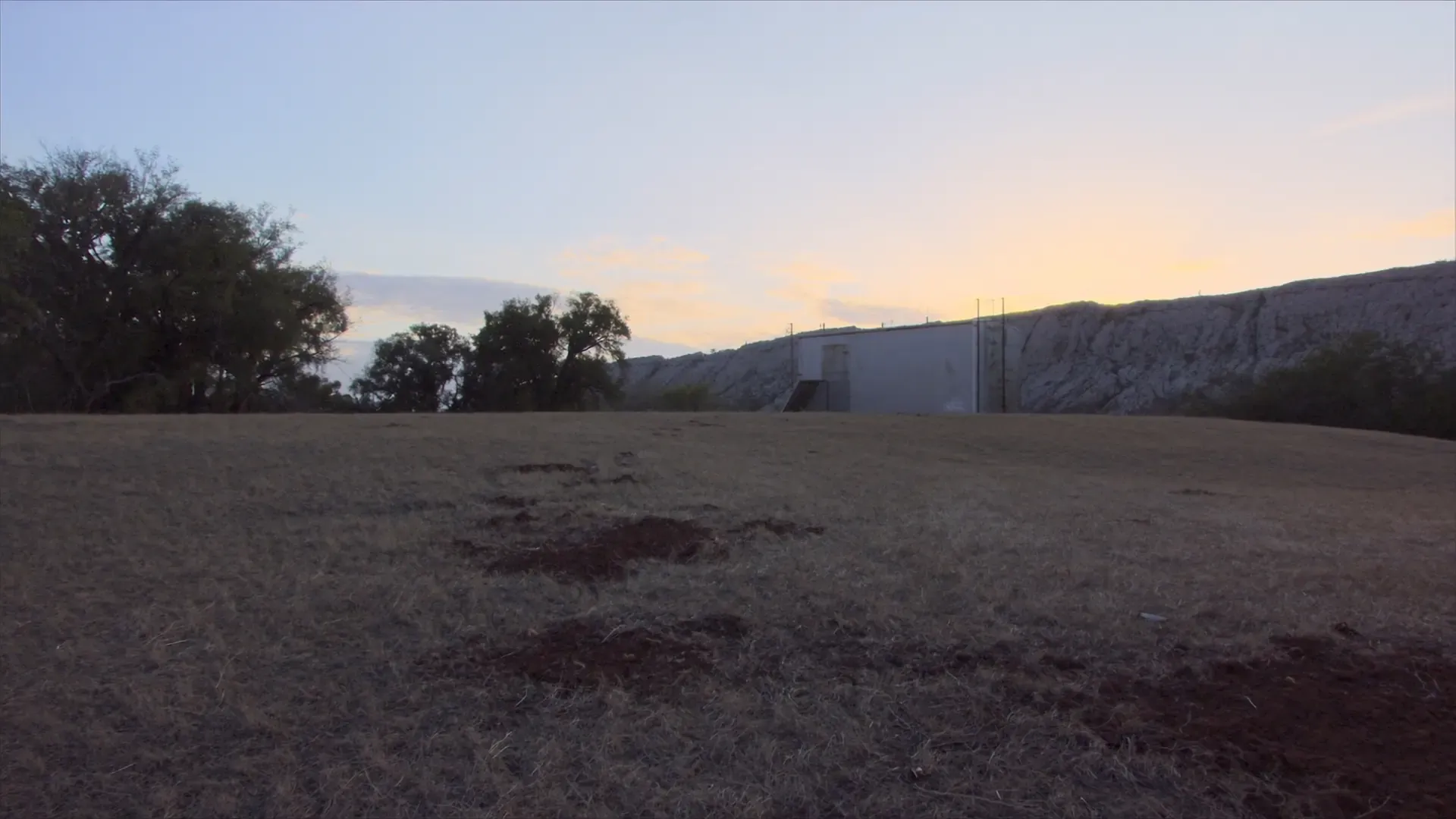 A metal building across a dry grass field at dusk near Austin, Texas
